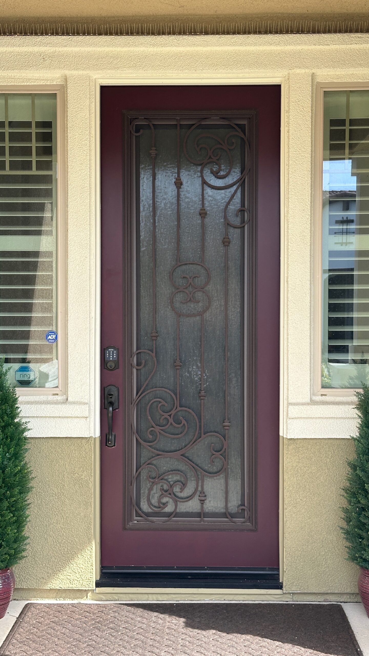 Residential entryway featuring a decorative burgundy door with wrought iron detailing, framed by light-colored walls and flanking potted shrubs, symbolizing quality home exterior painting services in El Dorado Hills, CA.